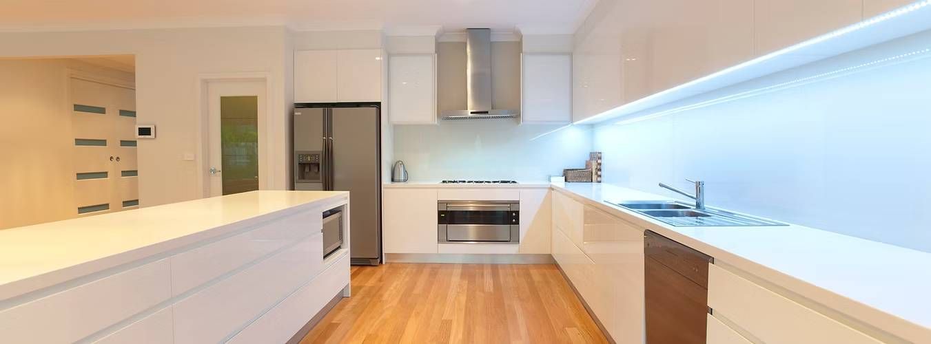 Modern kitchen with sleek white cabinets, stainless steel appliances, and wooden floors
