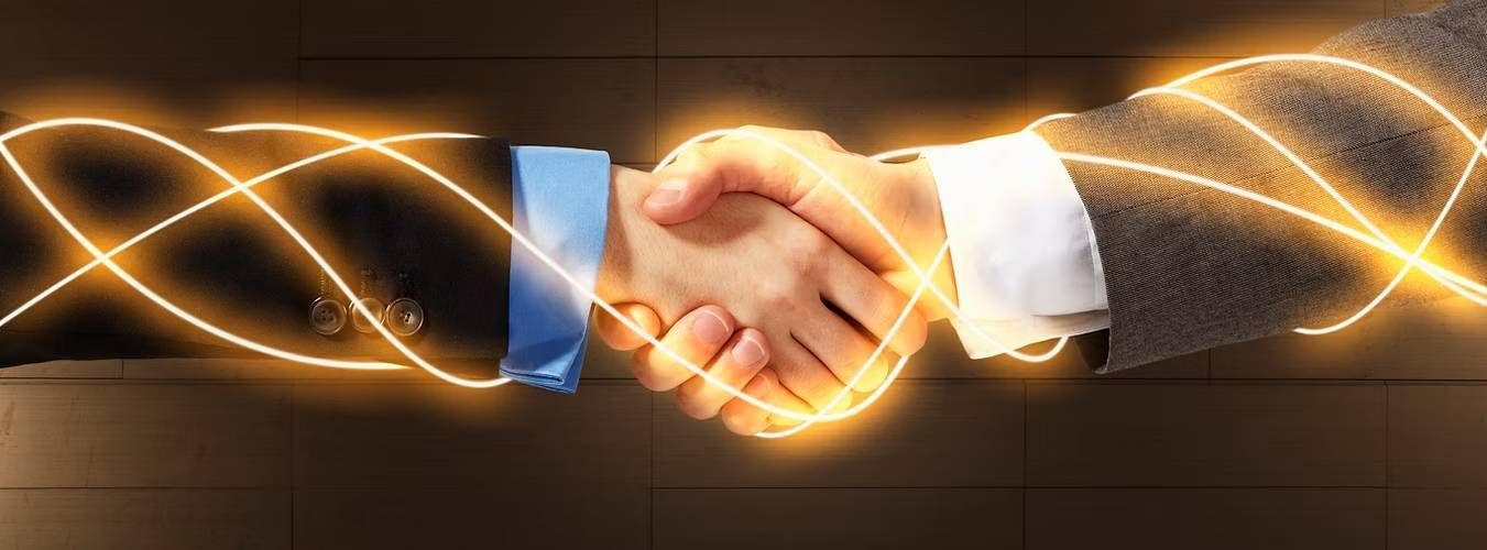Two hands in business suits shake with warm yellow light trails
