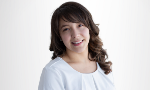 Smiling woman with shoulder-length dark hair in a white top against a light background