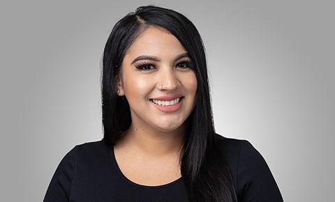 Smiling person with long black hair wearing a black top against a gray background
