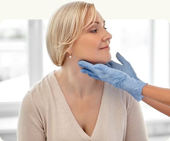 Medical professional examining a woman’s neck with blue-gloved hands in a bright clinic