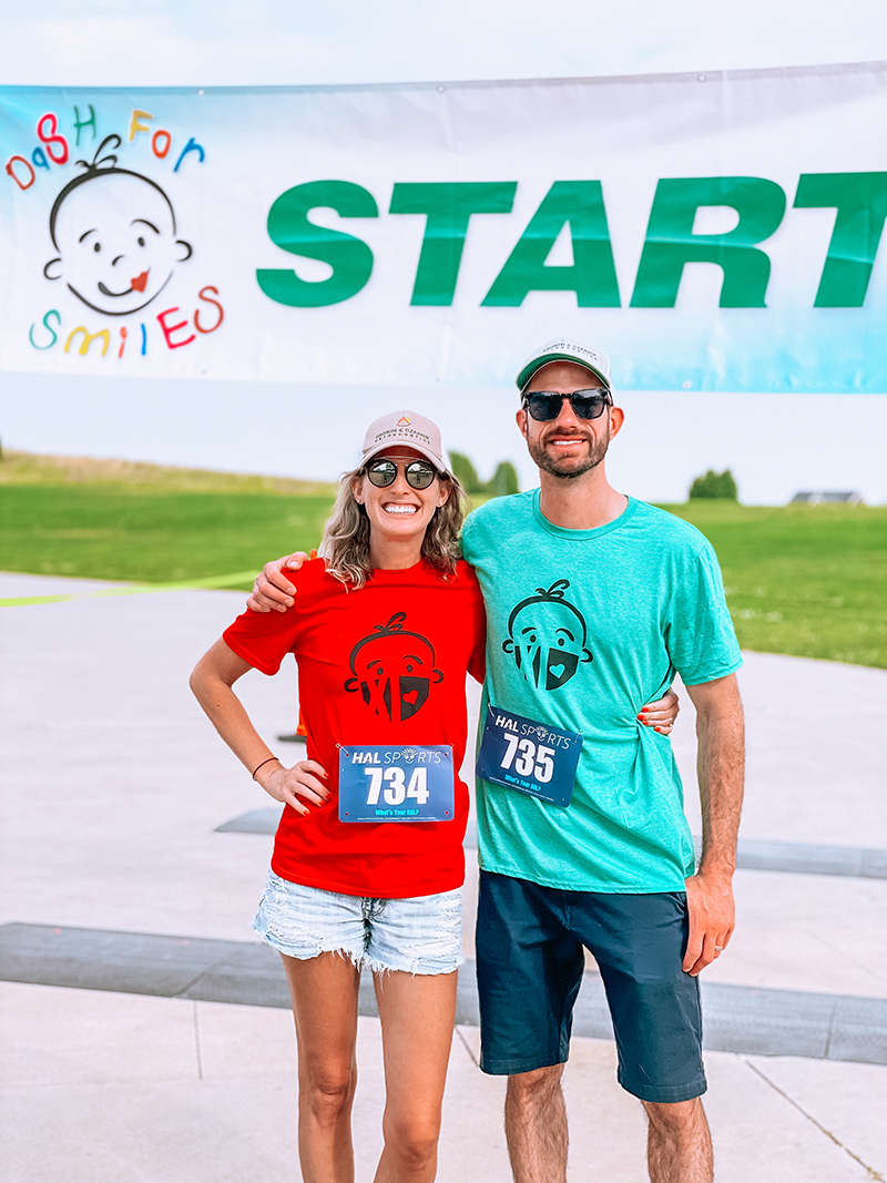 Two runners in red and teal shirts standing at a race start line banner.