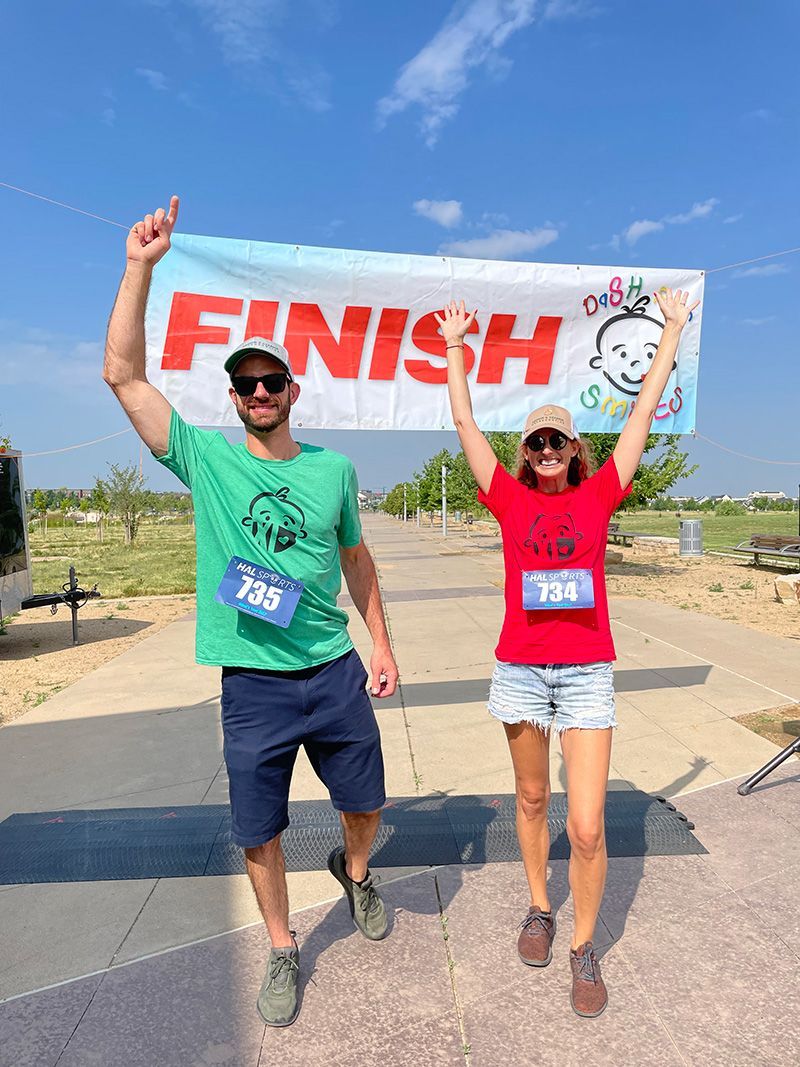 Two runners cross a finish line outdoors, arms raised under a “FINISH” banner.