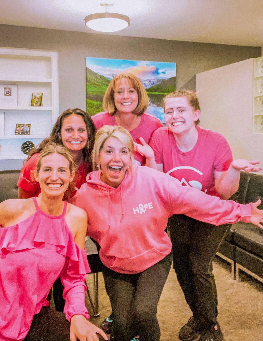 Five people in pink sweatshirts smile and pose indoors in a living room.