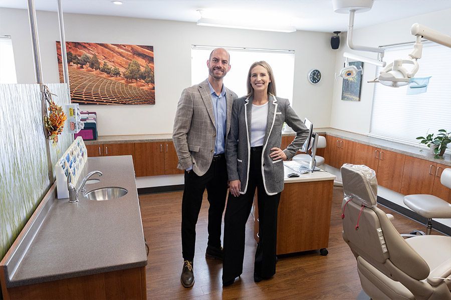 Two people standing in a modern dental office, smiling beside a dental chair.