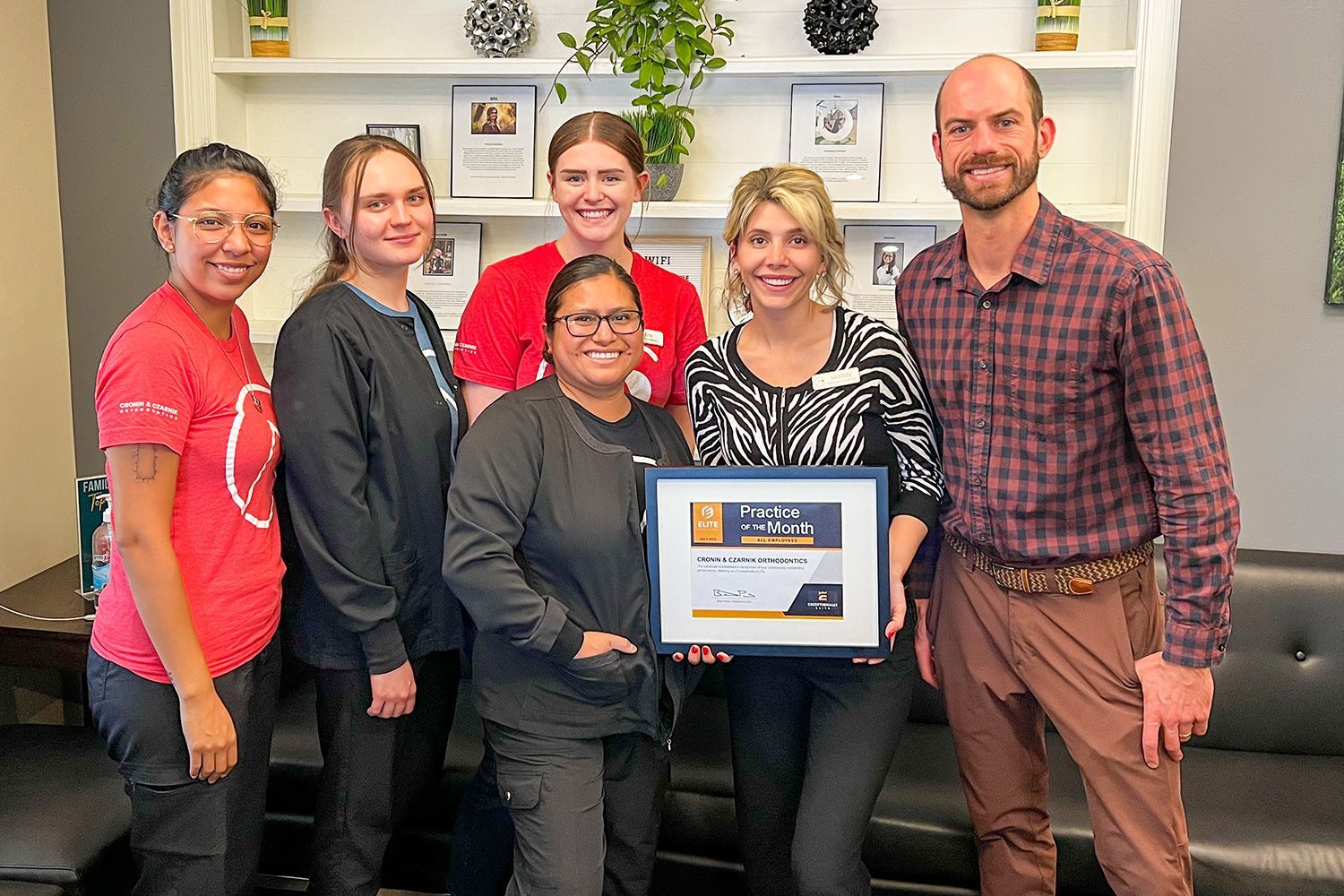 Six people pose in an office, with one holding a framed certificate.