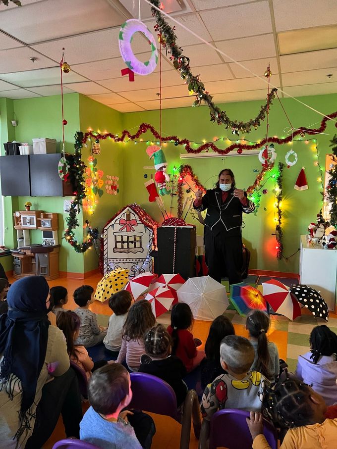 Un groupe d'enfants sont assis sur des chaises dans une pièce décorée pour Noël.