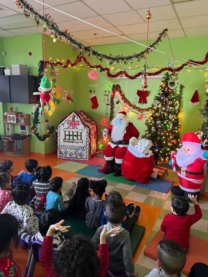 Un groupe d'enfants sont assis dans une pièce avec le Père Noël et un sapin de Noël.