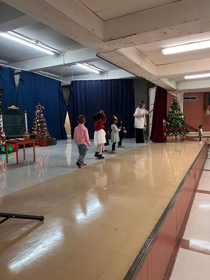 Un groupe d'enfants se tient sur une scène dans une pièce avec des sapins de Noël.