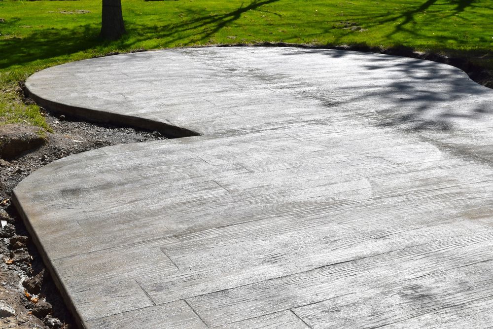 Newly poured gray concrete patio with curved edges in a grassy yard.