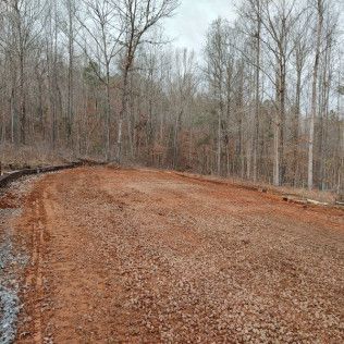 Red dirt clearing in a forest with bare trees, possibly prepared for construction.
