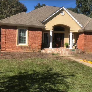 Red brick and stucco house with brown roof and lawn.