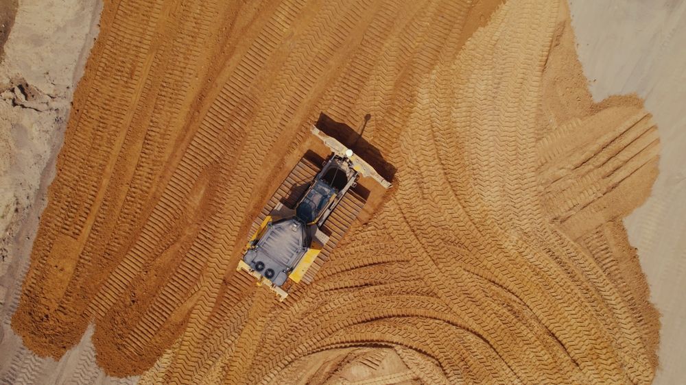 A construction machine leveling out a large pile of sand or gravel outdoors.