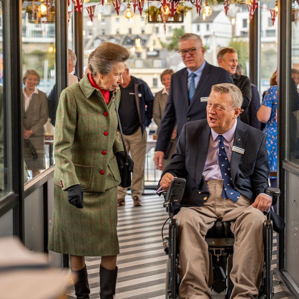 Princess Anne greets a man in a wheelchair on a boat. Other people watch.