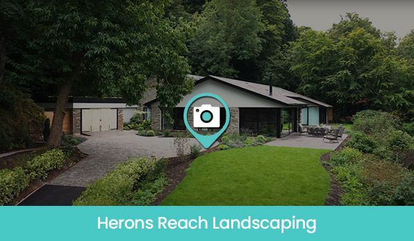 Landscaped house exterior with driveway, green lawn, and surrounding trees. 