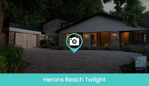 Twilight photo of a house with a gravel driveway, garage, and gardens. A camera icon is superimposed.