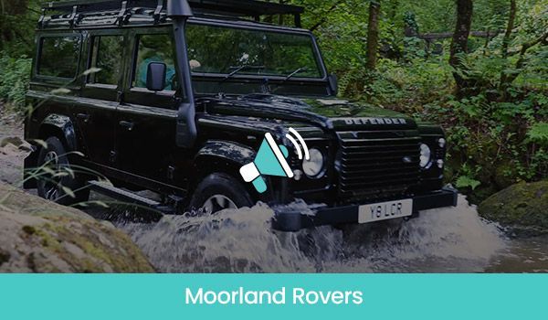 Black Land Rover Defender fording a stream in a forest setting;