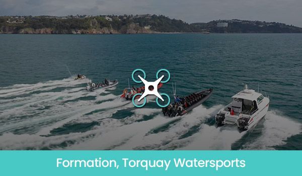 Boats in formation on the water near Torquay. Drone icon overlayed. Turquoise sea, green land in background.