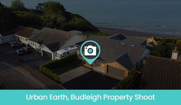 Aerial view of homes with a beach and ocean backdrop. Teal location marker. “Urban Earth, Budleigh Property Shoot” text.