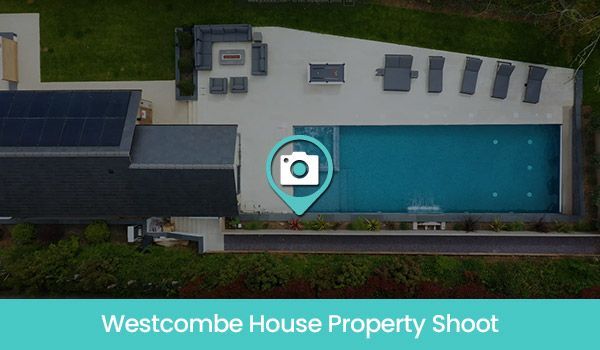 Aerial view of Westcombe House with pool, outdoor seating, and solar panels. Turquoise accent overlay.