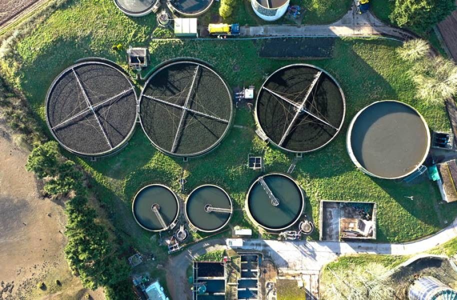 Aerial view of a wastewater treatment plant with several circular tanks filled with dark material.