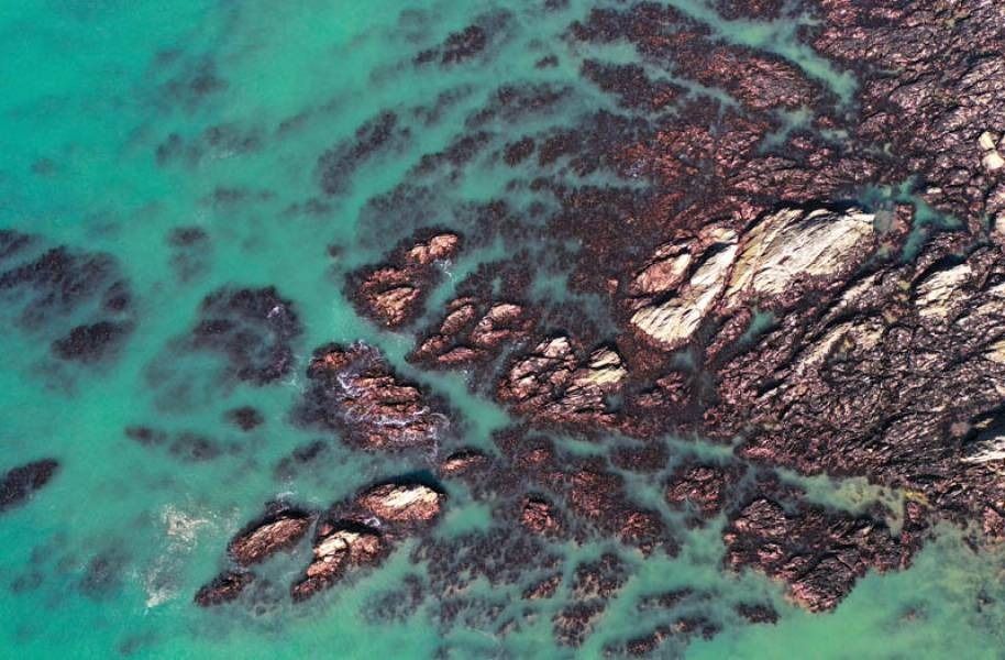 Aerial view of turquoise water surrounding dark, rocky formations.