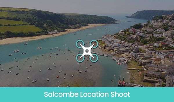 Aerial view of Salcombe estuary with drone icon, turquoise water, boats, and waterfront buildings.