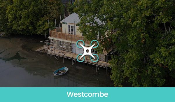 A house on stilts at the water's edge, drone icon overlaid, teal text: Westcombe.