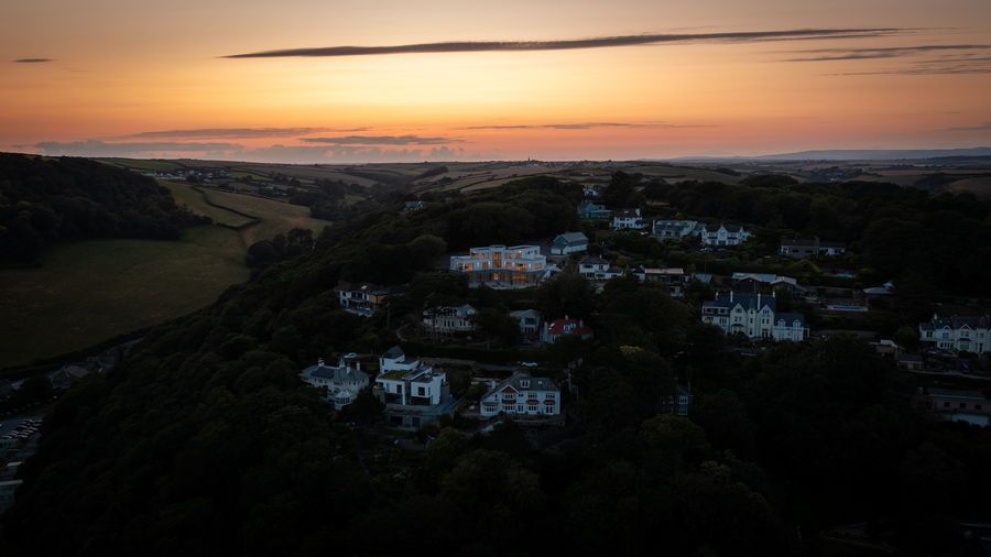 Dusk view of a village nestled in a valley, with houses and trees under an orange and yellow sky.