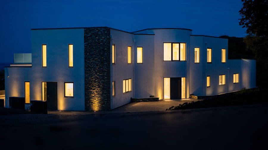 Modern white house with illuminated windows and stone accent at night.