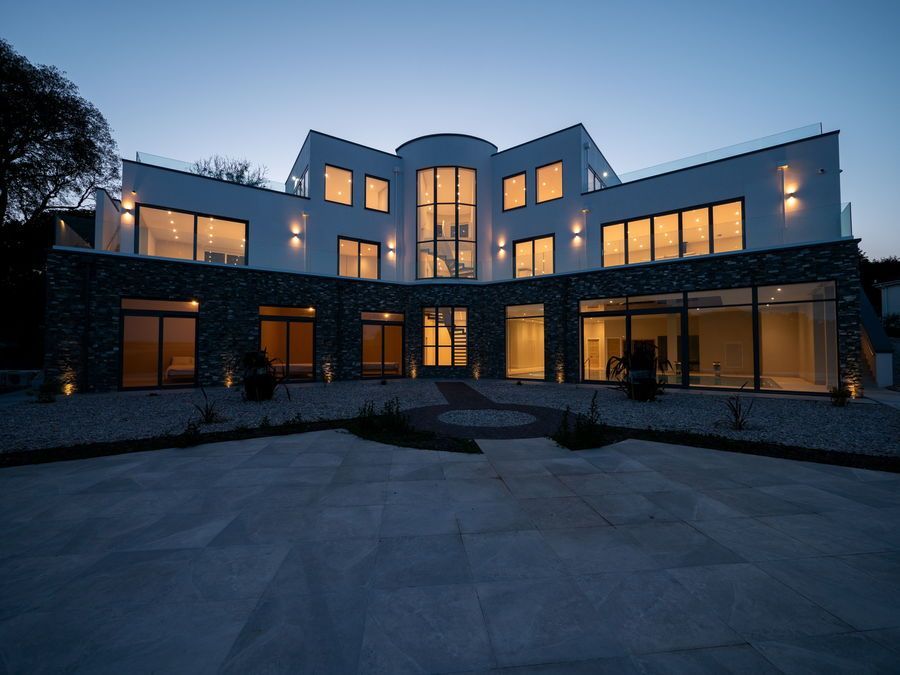 Modern multi-story white house with large windows, stone accents, and exterior lighting at dusk.