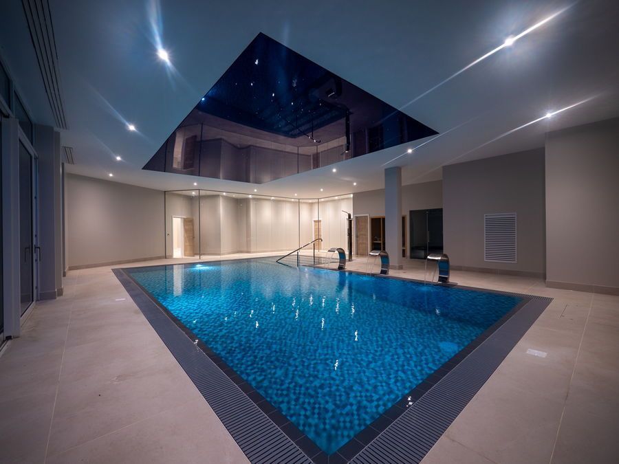 Indoor swimming pool with blue tiled water, silver ceiling, and recessed lighting.