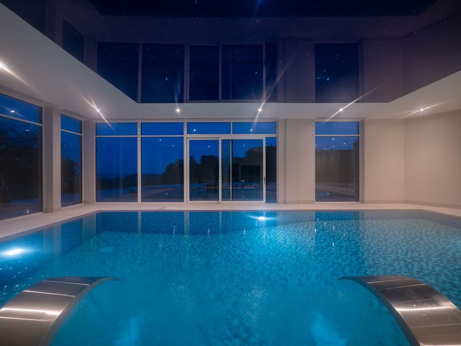 Indoor pool with blue water, large windows, and a dark ceiling.