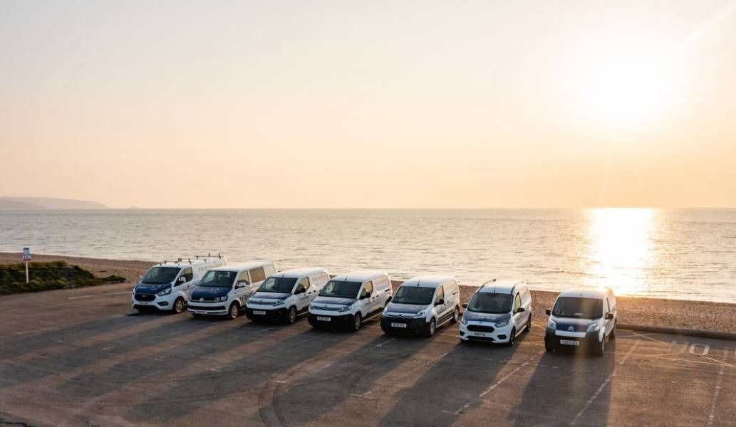 Lineup of vans parked on a concrete platform near the beach during sunset.
