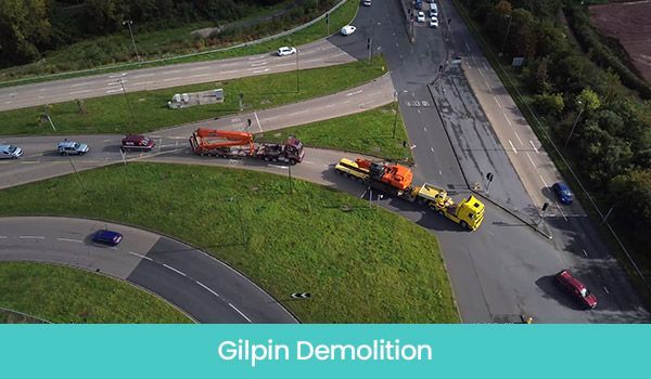 Aerial view of Gilpin Demolition vehicles at an intersection, with cars on nearby roads and green grassy areas.