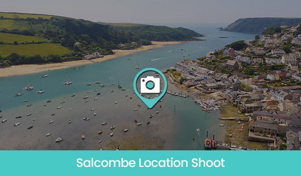 Aerial view of Salcombe estuary with a teal-colored water, small boats, and a seaside town.
