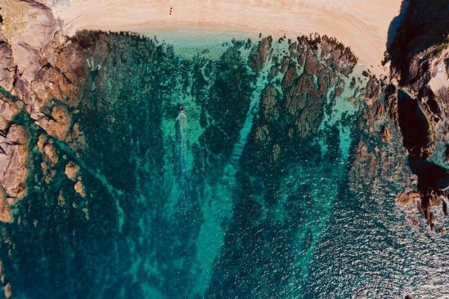 Aerial view of clear turquoise water meeting a sandy beach and rocky shore.