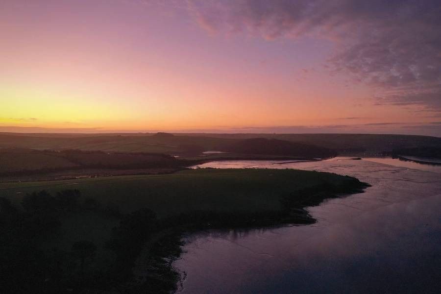 Sunset over a river and landscape, with purple and orange hues in the sky.