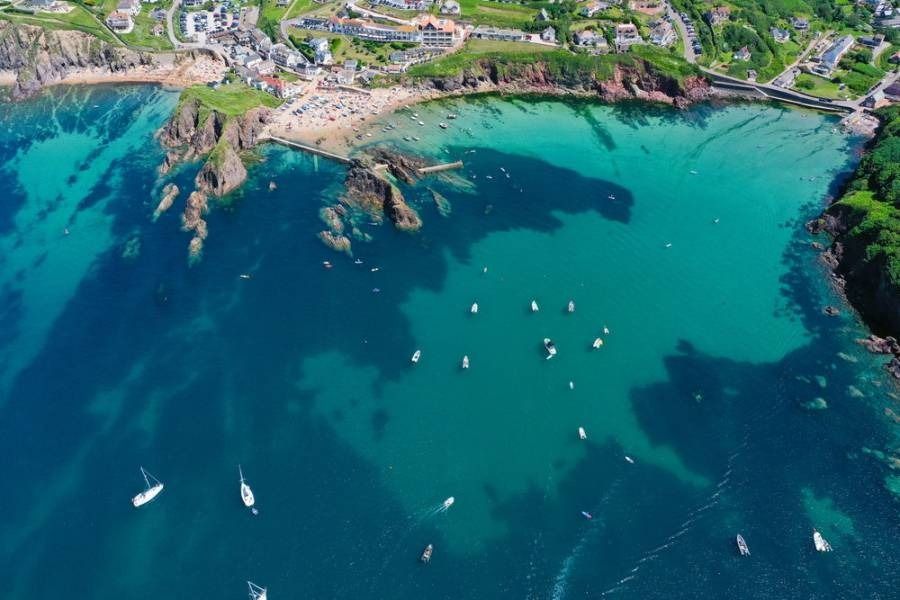 Aerial view of turquoise bay with boats, beach, and green cliffs.