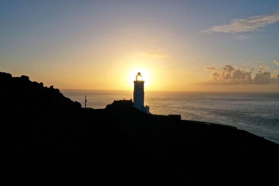 Lighthouse silhouetted against a sunrise over the ocean.