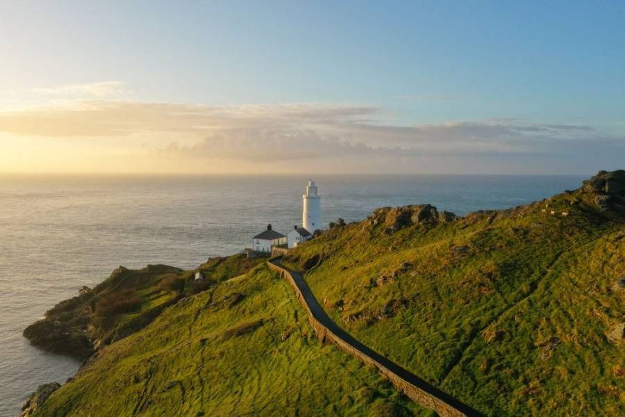 Lighthouse on a grassy cliff overlooking the ocean at sunrise.