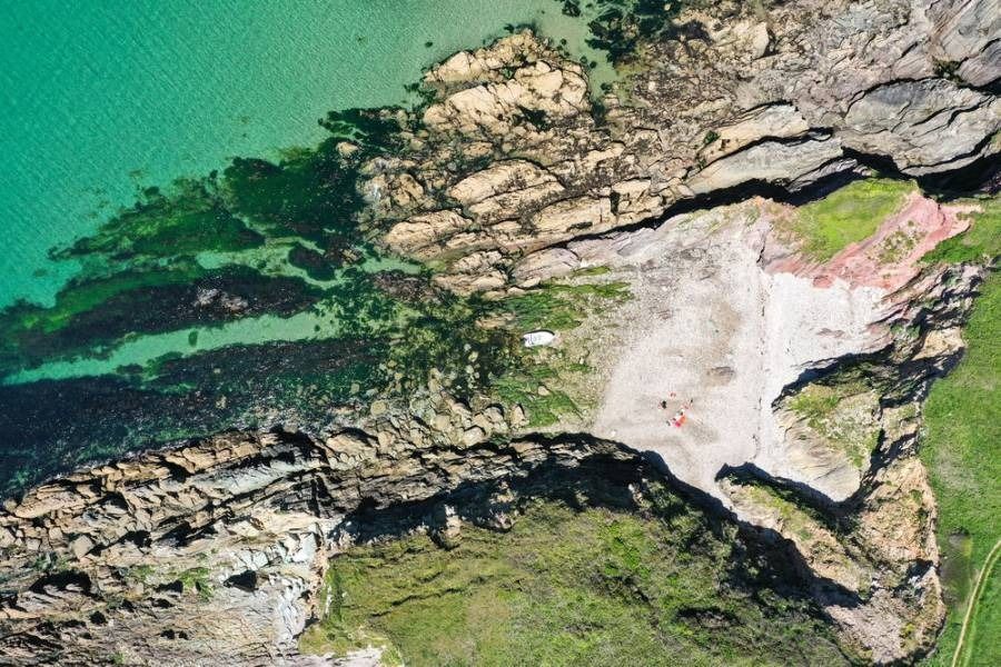 Aerial view of rocky coastline with turquoise water, a small beach, and green grass.