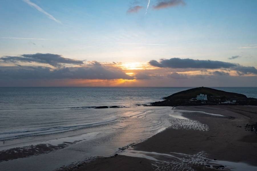 Beach at sunset, sun behind clouds over the ocean, small island with a white building.