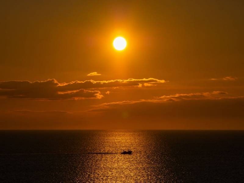 Golden sunset over ocean, small boat sailing on shimmering water.