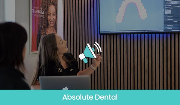 A dental professional points to a screen showing a 3D dental model while speaking to a client in a modern office.