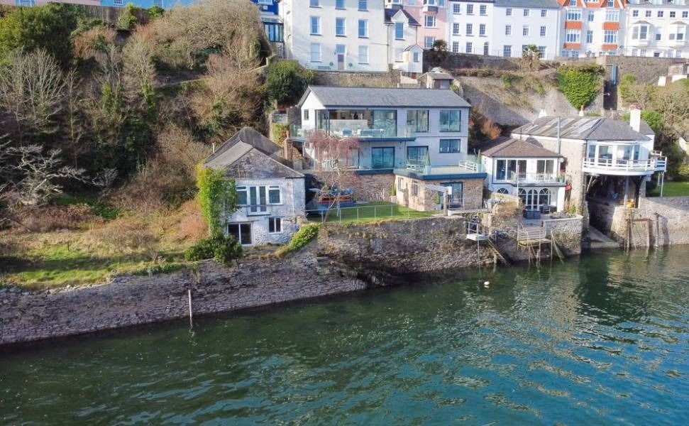 Waterfront houses on a hillside, overlooking a calm body of water. Green vegetation, cloudy sky.