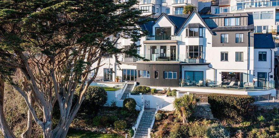 Luxurious white house with black accents, overlooking a hillside with stairs and trees.