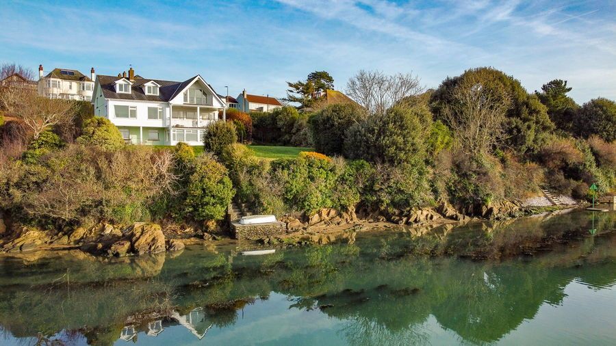 White house on a green cliff overlooking calm, teal water with reflections. Blue sky.