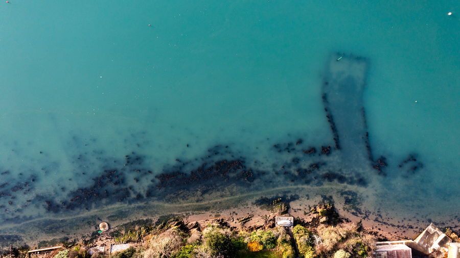 Aerial view of a teal-colored shoreline with an old submerged pier.