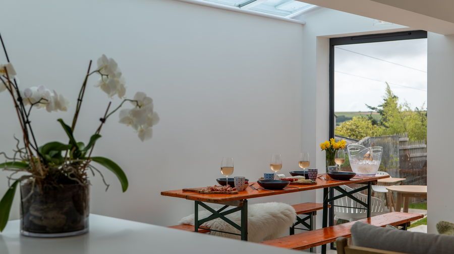 Dining area with orange picnic table, white walls, and outdoor view. Orchid flowers in foreground.